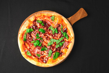 Fresh tasty pizza on black background. Traditional Italian pizza with grilled sausages and arugula over black.