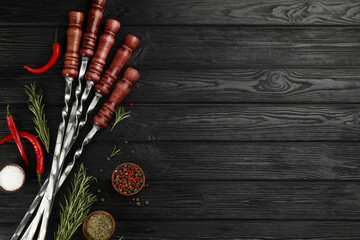 Flat lay composition with metal skewers on black wooden table. Space for text
