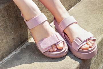 Female feet in pink sandals on concrete background close-up.
