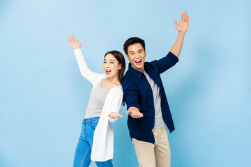 Surprised Asian couple standing back to back smiling and opening hands in light blue isolated...