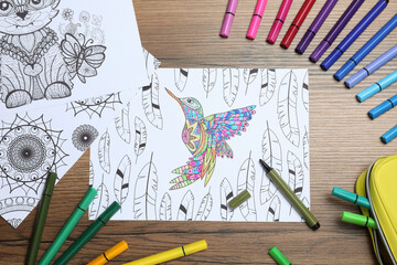 Antistress coloring pages and felt tip pens on wooden table, flat lay