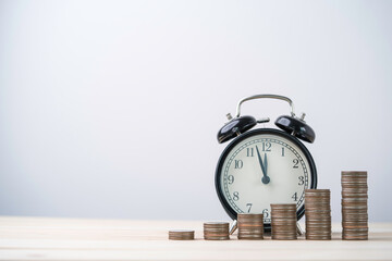 Coins stacking with alarm clock on wooden table , time and money management concept.