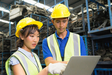 Man and woman work together, diversity of Asian engineer workers stand and seriously using laptop in factory-warehouse
