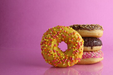 Sweet still life donut berliner close-up at the back lie a stack of three doughnut chocolate pink yellow on a bright pink fuchsia background with a place for text for a cafe for tablecloths for glue