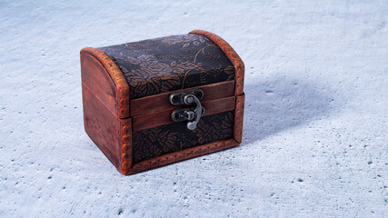 Small old brown wooden treasure chest on a gray plastered surface. Isolated vintage locked jewelry box.