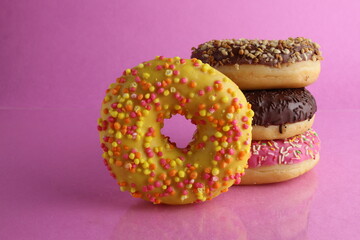 Sweet still life donut berliner close-up at the back lie a stack of three doughnut chocolate pink yellow on a bright pink fuchsia background with a place for text for a cafe for tablecloths for glue
