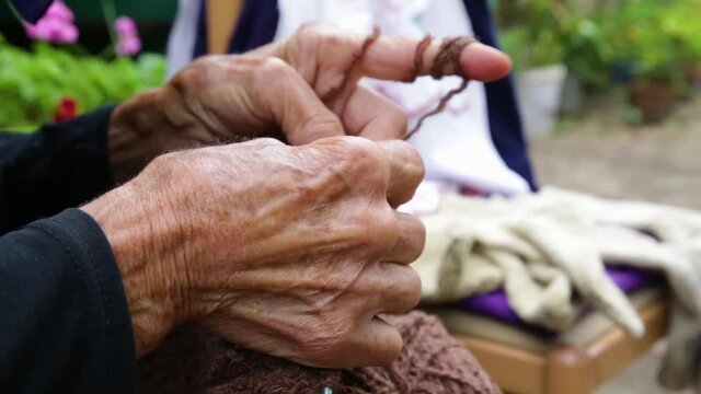 Grandma with wrinkled hands knits in her yard