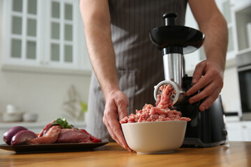 Man using modern meat grinder in kitchen, closeup