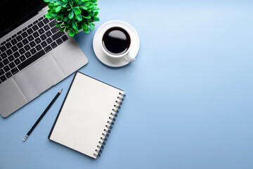 Flat lay, top view office table desk. Workspace with, laptop,office supplies, pencil, green leaf, and coffee cup on blue background.