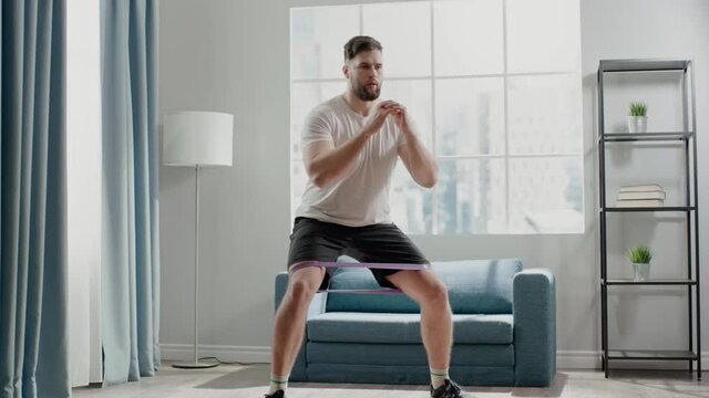 Active sportsman steps in half squat with elastic belt