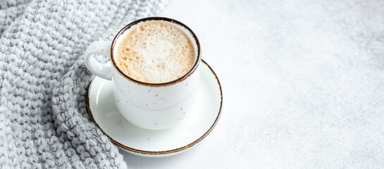 White mug with coffee and wool scarf on stone background. Winter composition in scandinavian style. Copy space for text