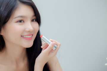 Beautiful young asian woman applying lipstick pink with style bright and shiny on mouth, beauty girl looking mirror for makeup cosmetic with lip elegance, fashion make up with luxury and sexy.