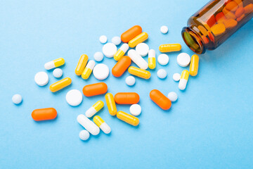 Multicolor tablets and pills capsules from glass bottle on blue background Close-up