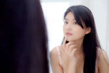 Beautiful young asian woman smiling look at mirror of checking face with skin care and cosmetic for...