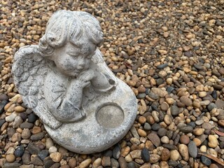 Little cute cupid angel sculpture on river gravel background in the english  garden.