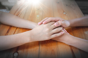 Hands of husband and wife are praying together on wooden table in home, Christian family concept.