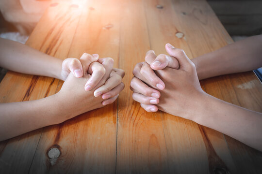 Hands of two christian praying together on wooden table at home, Christian concept.