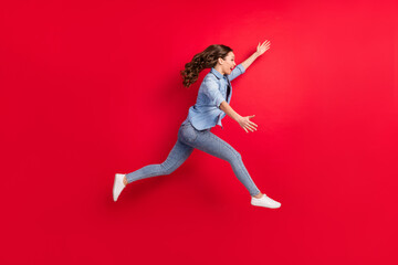 Full length body size side profile photo of cheerful girl jumping up running catching isolated vibrant red color background