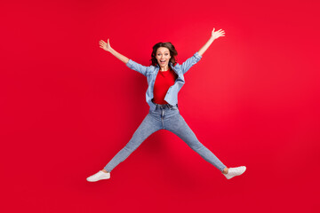Photo of shiny adorable young woman wear jeans shirt smiling jumping high like star isolated red color background