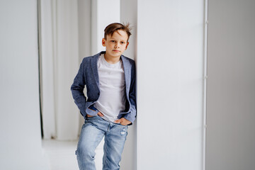 Fototapeta na wymiar A teenage boy in a jacket and jeans poses standing by a window. 