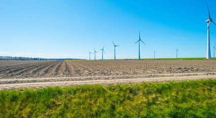 Wind turbines for renewable energy in an agricultural field in bright blue sunlight in spring, Noordoostpolder, Flevoland, The Netherlands, April 26, 2021