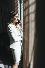 Fototapeta premium Young brunette woman business lady in white suit with mobile in hotel room