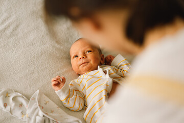 Mom dresses cute newborn little baby boy in a  jumpsuit. Happy young mother playing with baby while...
