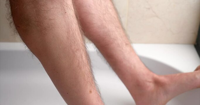 close up view of man shaving his leg in the bathroom at home