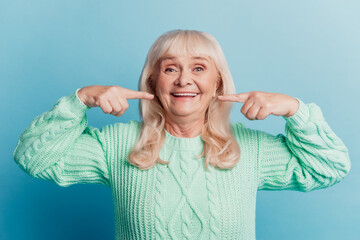 Photo of happy with beaming smile woman pensioner point white teeth isolated on blue background