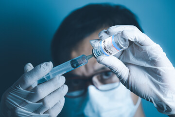 A man's hand wearing medical gloves. Using a cyring inserted into a covid-19 vaccine bottle against a blurry background.