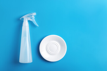 Blue dishwashing background with dish spray bottle and clean white glass plate on blue background. Top view, copy space.