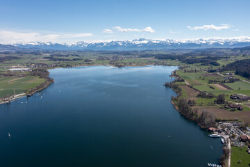 Luftaufnahme vom Greifensee im Vordergrund und den schneebedeckten Bergen der Alpen im Hintergrund, Zürich, Schweiz