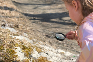 Little girl with a magnifying glass in her hand investigate  details of stone covered with moss or...