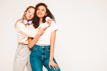 Two young beautiful smiling international hipster female in trendy summer clothes.Sexy carefree women posing on grey background in studio.Positive models having fun.Concept of friendship
