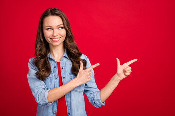 Portrait of attractive cheerful wavy-haired girl demonstrating aside copy space ad offer isolated over vibrant red color background