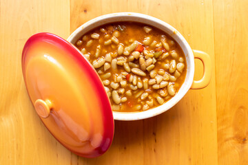 Guiso de almejas y judías asturianas servido en un cuenco de naranja. Cocina española. Enfoque selectivo. Fabes con marisco.