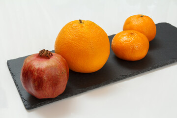 Pomegranate, orange and tangerines on the black stone board.