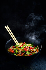 Rice noodles with vegetable stir fry on the ceramic plate on dark background