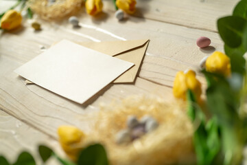 Spring Easter holiday. top view background with eggs in nests, yellow tulips and an envelope with card for writing, on light wooden table with natural sunlight. Greeting card background. copy space.