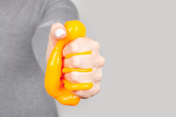 Hand with yellow slime toy on grey background