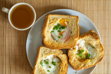 Morning breakfast. Fragrant baked sandwiches with egg, ham, cheese and pickles lie on a plate on the table, next to a mug of green tea in the kitchen on the table with morning sunlight. top view