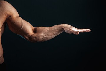 Obraz na płótnie Canvas tense arm, veins, bodybuilder muscles on a dark background, isolate