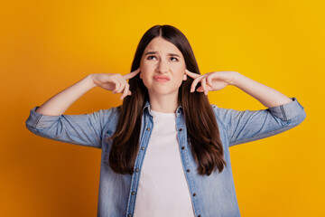 Portrait of annoyed woman fingers close ears look empty space on yellow background