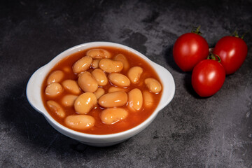 White falo in tomato sauce. Boiled beans, stewed with tomato sauce on a white dish on a dark surface. Close-up