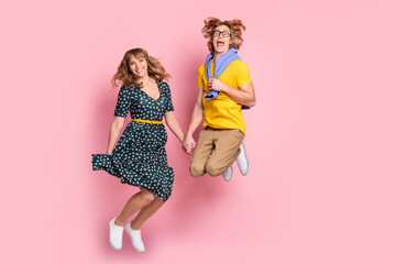 Full length body size photo of funny couple jumping spending time together keeping hands isolated on pastel pink color background