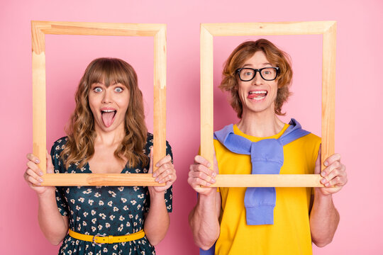 Photo of young happy funky funny playful couple hold wooden frames showing tongue isolated on pink color background
