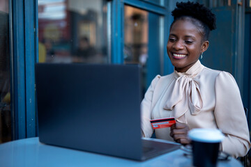 African businesswoman in cafe makes a purchase on the Internet. Beautiful woman on the laptop with credit card..