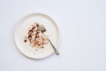 Dirty plate with cake leftovers and fork on white background, top view