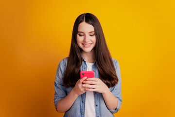 Portrait of lovely cheerful girl holding in hands smartphone look screen chatting toothy smile