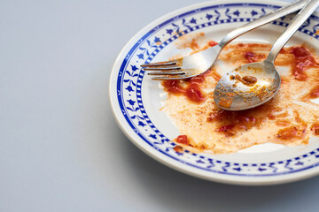 Empty dirty plate with spoon and forks on gray background